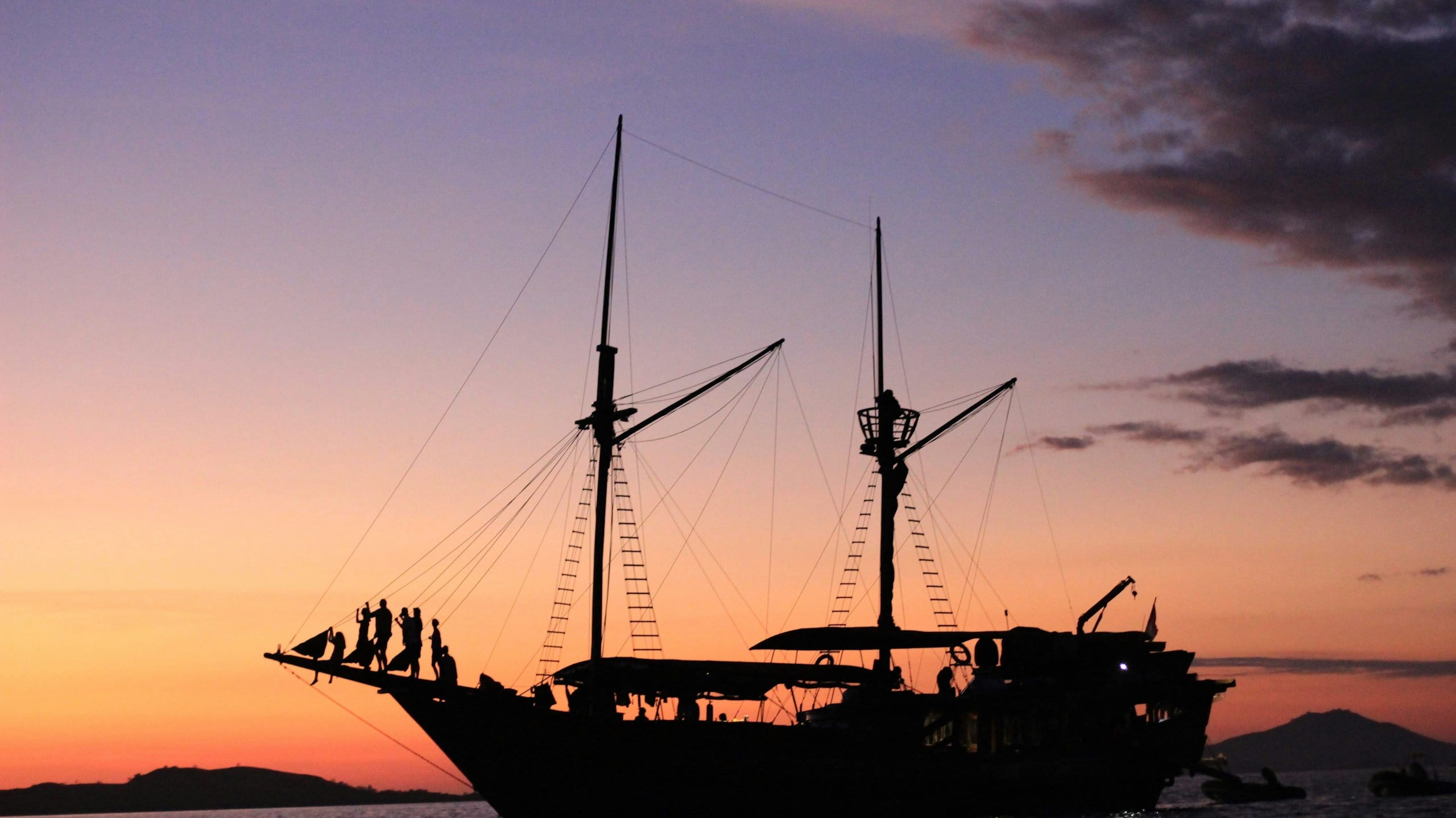 Travellers on the bow of a phinisi boat at sunset in Labuan Bajo